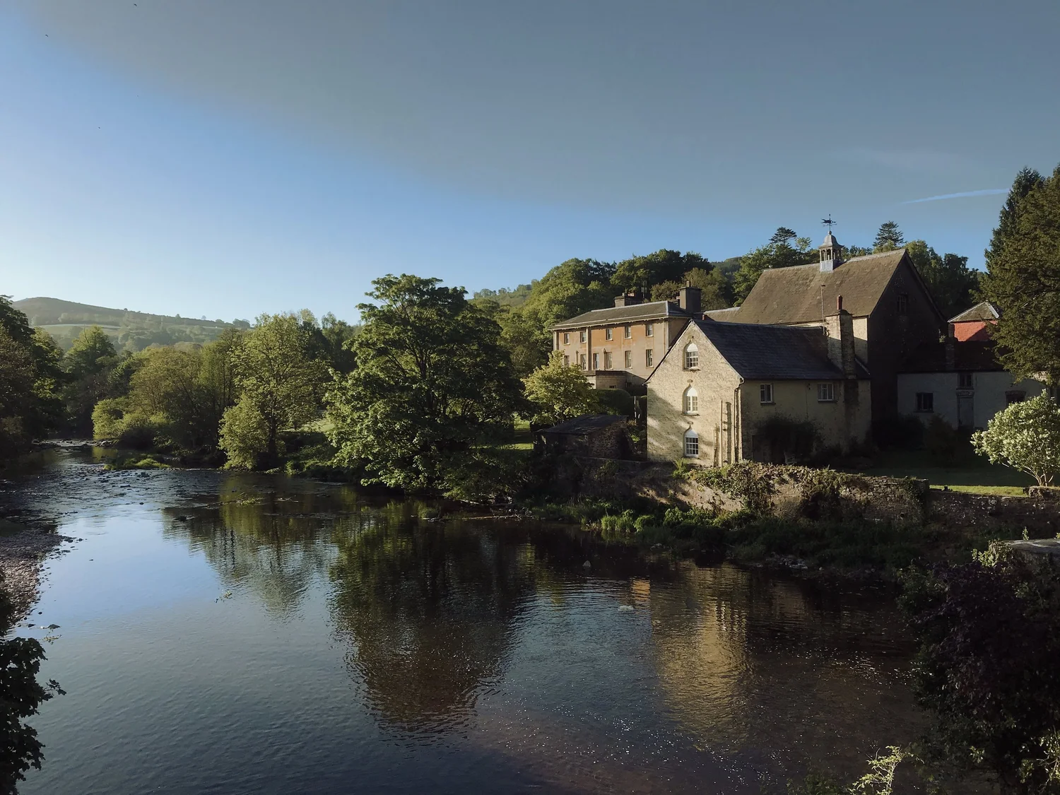Penpont’s buildings beside the River Usk, surrounded by trees.